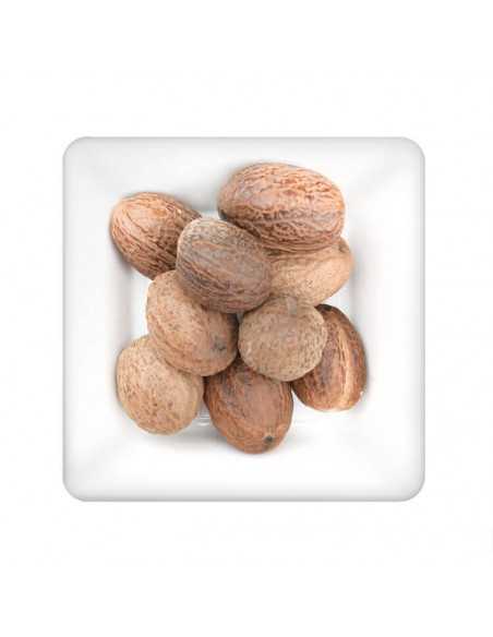 Ganze, hellbraune Muskatnüsse auf weißem, quadratischem Teller.