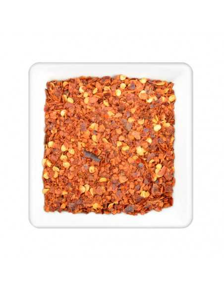 Rote, grob geschrotete Chilistückchen mit vereinzelten gelben Samenkörnern auf weißem Teller quadratisch angerichtet.