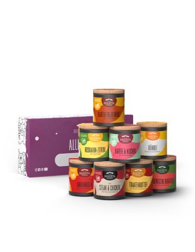 Acht bunte Bio-Pappdosen vor lilafarbener Geschenkbox mit dem Schriftzug „Alles Gute!“ und einem Namensfeld.