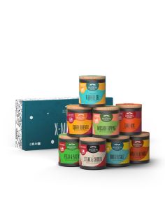 Acht bunte Bio-Pappdosen vor türkisfarbener Geschenkbox mit der Aufschrift „X-MAS-BOX“.