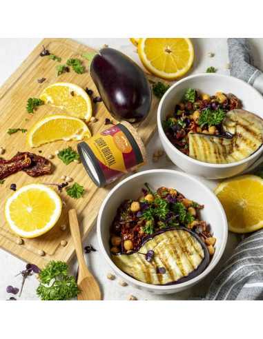 Schwarze Pappdose neben zwei Schalen mit Kichererbsen-Gemüsegericht, Auberginenscheiben, Petersilie und Orangenspalten