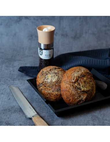Schwarze Schale mit zwei gewürzten Brötchen, daneben ein Messer; im Hintergrund eine Gewürzmühle mit schwarzem Etikett.