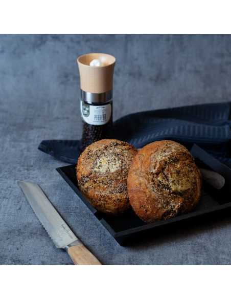 Schwarze Schale mit zwei gewürzten Brötchen, daneben ein Messer; im Hintergrund eine Gewürzmühle mit schwarzem Etikett.