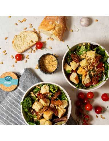 Zwei Schüsseln mit Brotsalat, daneben ein offenes Döschen Brotzeitsalz, Brot, Tomaten und Pinienkerne auf dem Tisch verteilt