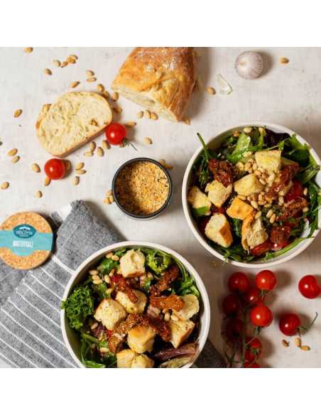 Zwei Schüsseln mit Brotsalat, daneben ein offenes Döschen Brotzeitsalz, Brot, Tomaten und Pinienkerne auf dem Tisch verteilt