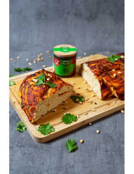 Schwarze Pappdose neben aufgeschnittenem Pizzabrot mit Pinienkernen und Koriander auf Holzbrett