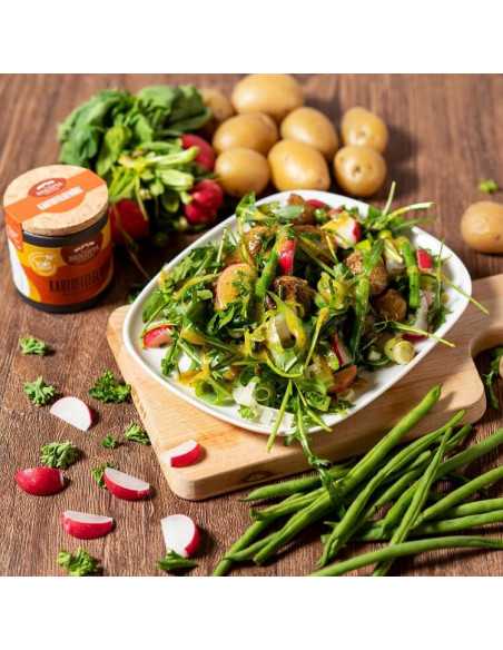 Schwarze Pappdose neben einem Kartoffelsalat mit Radieschen, Rucola, grünen Bohnen und Frühlingszwiebeln