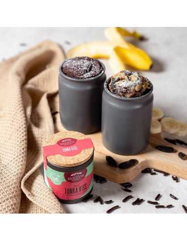 Schwarze Pappdose neben zwei dunklen Tassen mit gebackenen Schokoladen-Bananen-Desserts auf einem Holzbrett