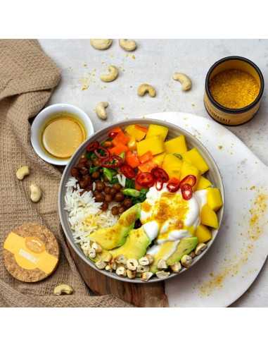 Geöffnete Pappdose neben einer Bowl mit Reis, Avocado, Paprika, Mango, Kichererbsen und Joghurt