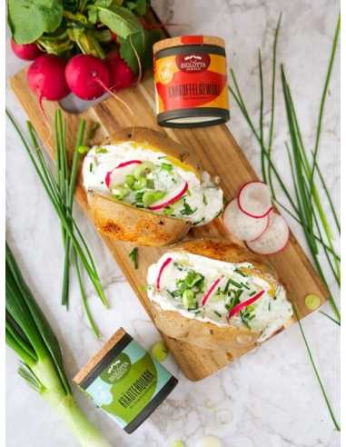 Schwarze Pappdose vor einer Ofenkartoffel mit cremigem Kräuterquark, Radieschenscheiben und Frühlingszwiebeln