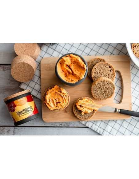 Schwarze Pappdose neben frischem Brot mit cremiger Tomatenbutter auf einem Holzbrett