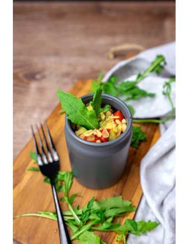 Grauer Keramikbecher mit Nudelsalat, dekoriert mit frischen Kräutern auf einem Holzbrett.