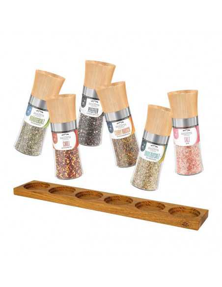 Sechs Gewürzmühlen mit Holzdeckel in verschiedenen Sorten, stehend vor einem Holzhalter mit Mulden.