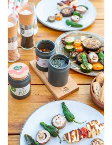 Gedeckter Holztisch mit Grillgemüse, zwei Keramiktöpfchen in Holzleiste und Biolotta-Gewürzen