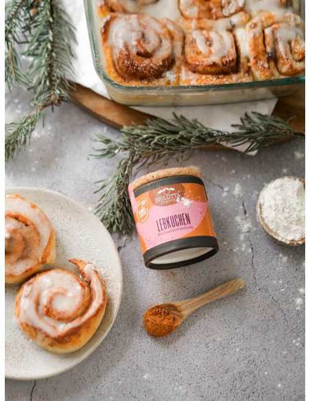 Schwarze Pappdose neben Zimtschnecken mit Zuckerguss, Holzlöffel mit Gewürzpulver und Tannenzweigen Schwarze Pappdose neben Zimtschnecken mit Zuckerguss, Holzlöffel mit Gewürzpulver und Tannenzweigen