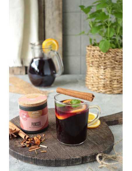 Schwarze Pappdose neben einer Glas­tasse mit rotem Punsch, Orangenscheiben, Zimtstange und Minze auf einem Holzbrett