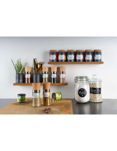 Küchenregal mit verschiedenen Gewürzmühlen und -gläsern, davor weitere Mühlen und Vorratsgläser mit „Mehl“ und „Hafer“.