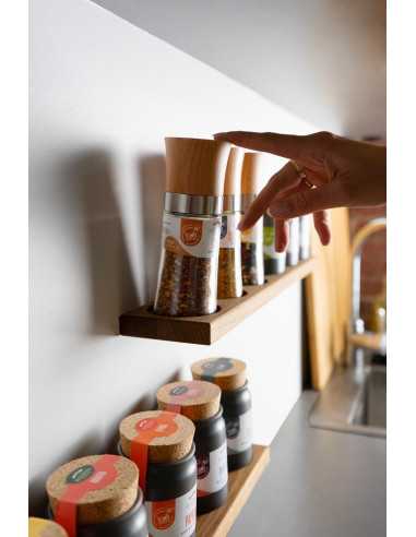 Küchenregal mit Bio-Mühlen und schwarzen Keramiktöpfchen, eine Hand greift nach einem Gewürzglas.