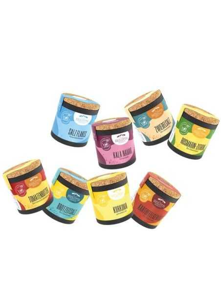 Acht bunte Bio-Pappdosen mit verschiedenen Gewürzen und Salzen, leicht versetzt nebeneinander stehend