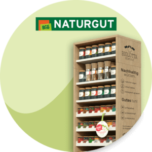Holzregal mit Biolotta-Gewürzen und Infotext zu Nachhaltigkeit, daneben das Logo „Naturgut Bio“ vor grünem Hintergrund.