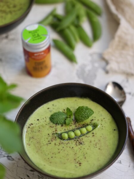 Erbsen-Minzsuppe, cremig püriert mit frischer Minze und BioLotta Curry Oriental, serviert in einer Schale mit Topping aus Erbsen und Minzblättern.