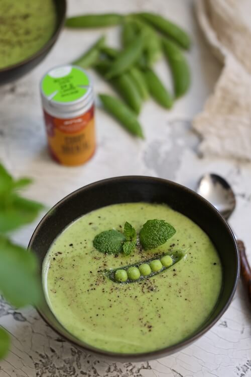 Erbsen-Minzsuppe, cremig püriert mit frischer Minze und BioLotta Curry Oriental, serviert in einer Schale mit Topping aus Erbsen und Minzblättern.