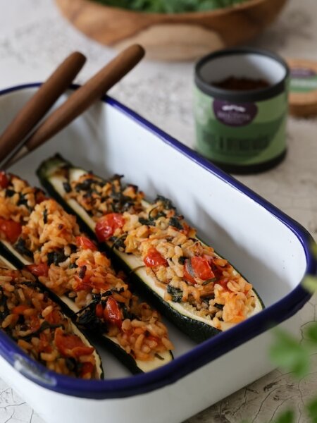 Gefüllte Zucchinihälften mit cremigem Tomaten-Risotto, Spinat und Parmesan in einer weißen Ofenform – sommerlich leichtes vegetarisches Gericht.