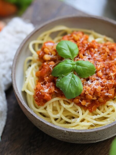 Vegane Linsen-Bolognese mit Spaghetti, garniert mit Basilikum, im Keramikschälchen, daneben italienische Kräutermischung von BioLotta.