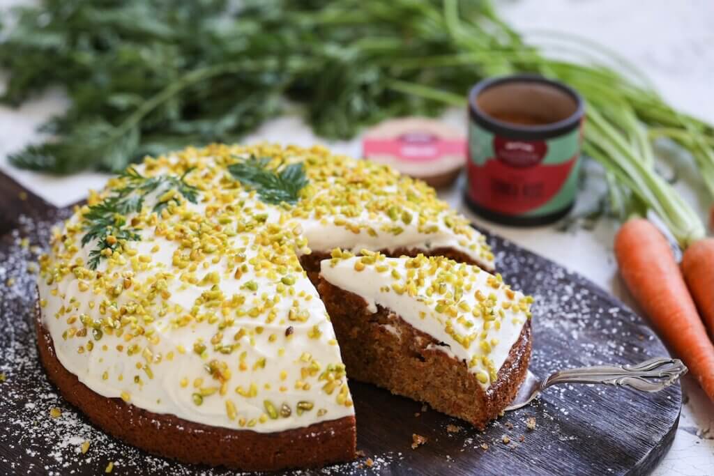 Saftiger Möhrenkuchen mit Frischkäse-Creme und gehackten Pistazien auf einem dunklen Holzbrett serviert