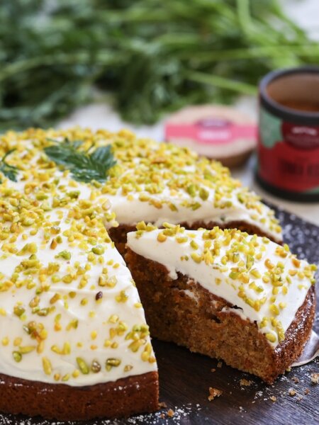 Saftiger Möhrenkuchen mit Frischkäse-Creme und gehackten Pistazien auf einem dunklen Holzbrett serviert